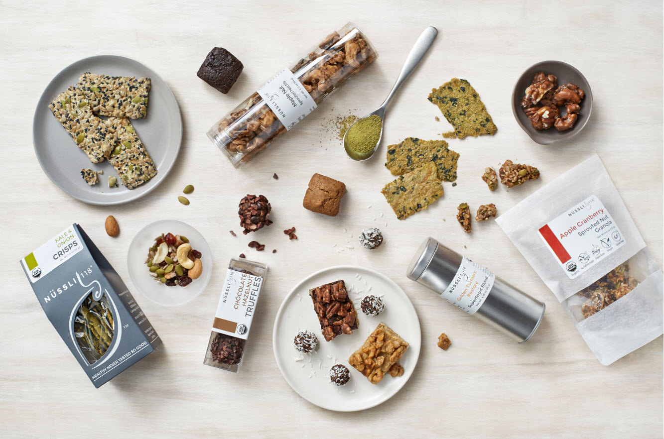 A variety of Nussli118 plant-based products including raw vegan sprouted nuts and seeds, superfood blends like matcha and ashwagandha, kale crackers, organic granola